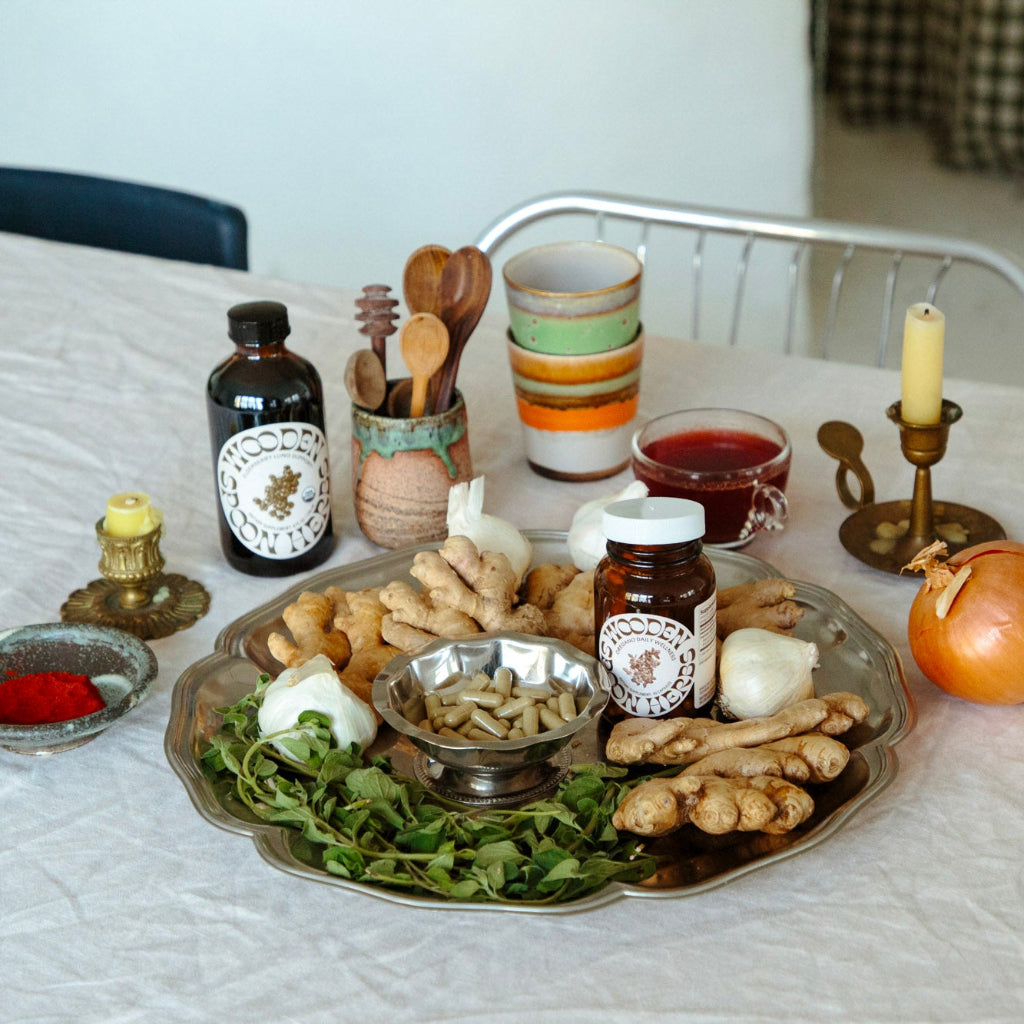 Table with Daily Immunity Duo from Wooden Spoon Herbs s including bottles, a candle, and a platter of food.
