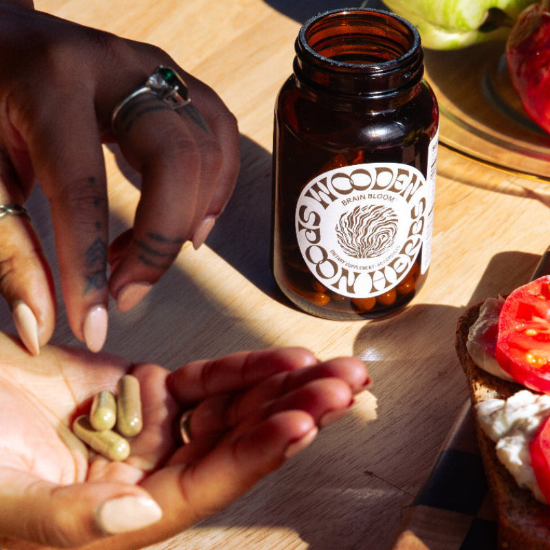 Person holding pills next to a bottle labeled 'Wooden Spoon Herbs' on a wooden surface.