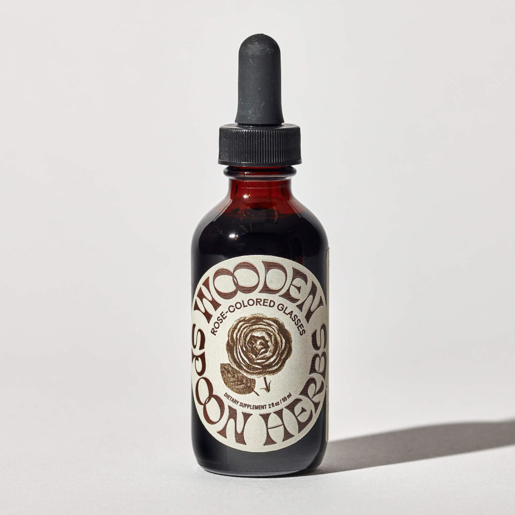 A bottle of 'Rose-Colored Glasses - Herbal Mood Support' tincture with a dropper, featuring a label with floral designs and the product name.